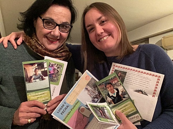 Two women, one older and one younger, hold up photos of their sponsored children, smiling at the camera.