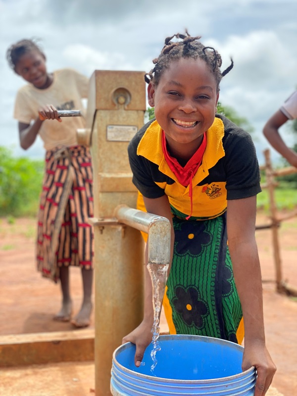 A girl in Mozambique smiles as she pumps fresh water from a well.