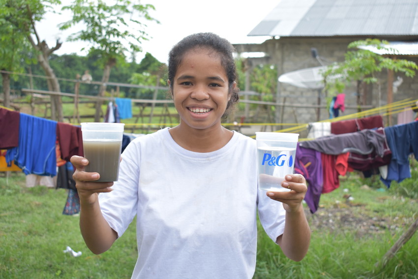 Young girl in Indonesia holds one cup of dirty water and one cup of clean water.