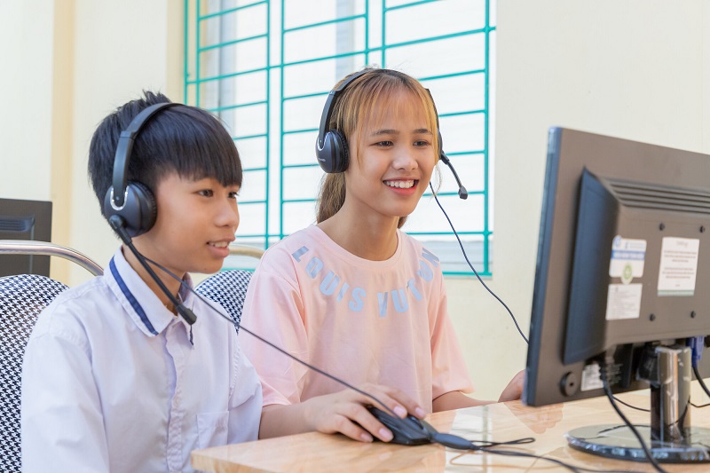 Boy and girl in Vietnam sit at a school computer, smiling.