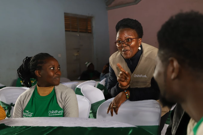 Woman in Kenya talks to a group of people seated at a table.