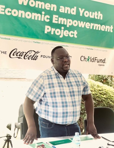 Man in Uganda stands at a table giving a speech.